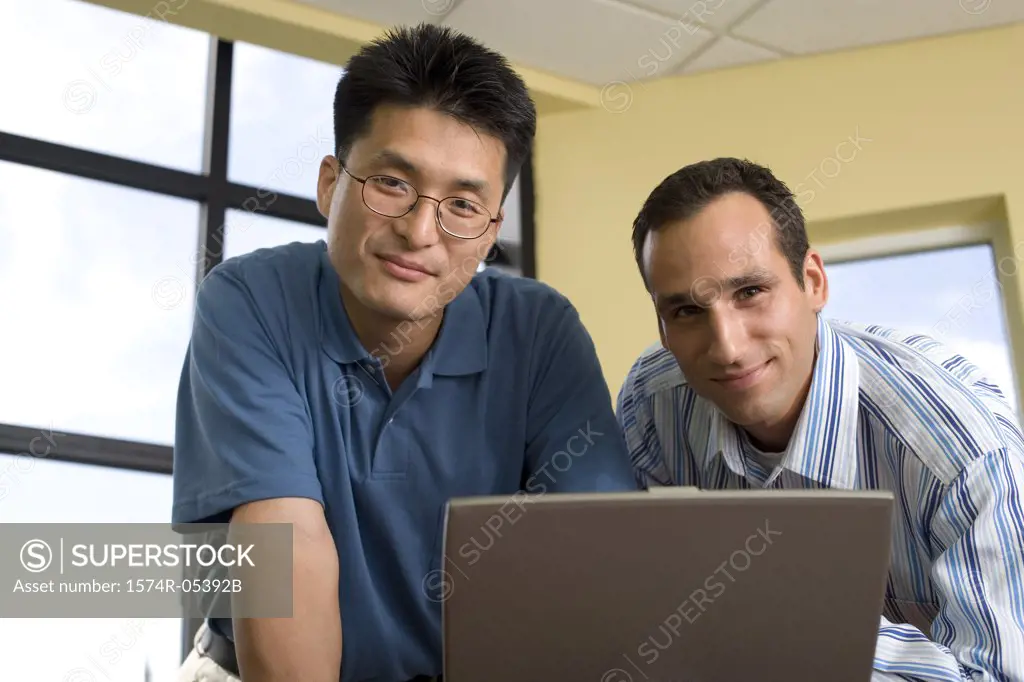 Portrait of two businessmen standing in front of a laptop in an office