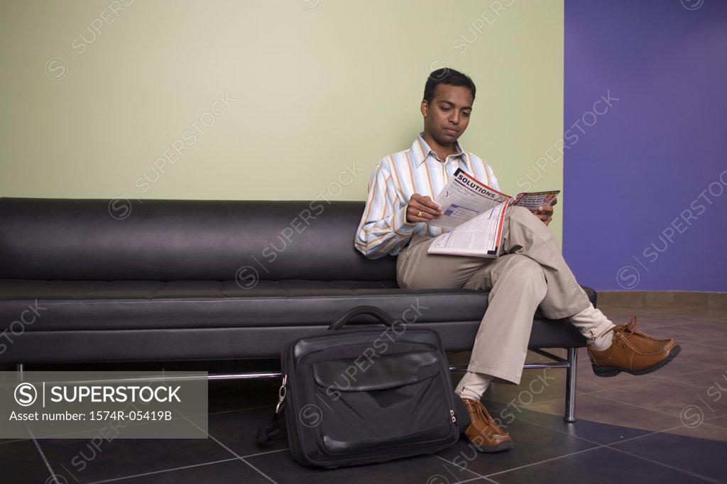 Stock Photo: 1574R-05419B Businessman sitting on a couch reading a magazine in an office