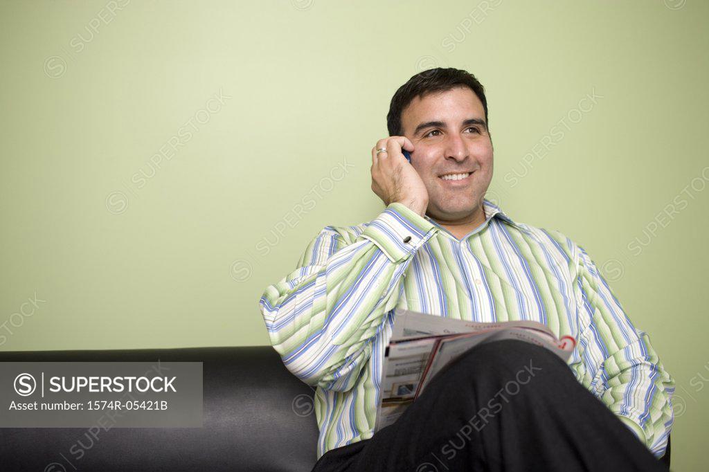 Stock Photo: 1574R-05421B Businessman sitting on a couch talking on a mobile phone in an office