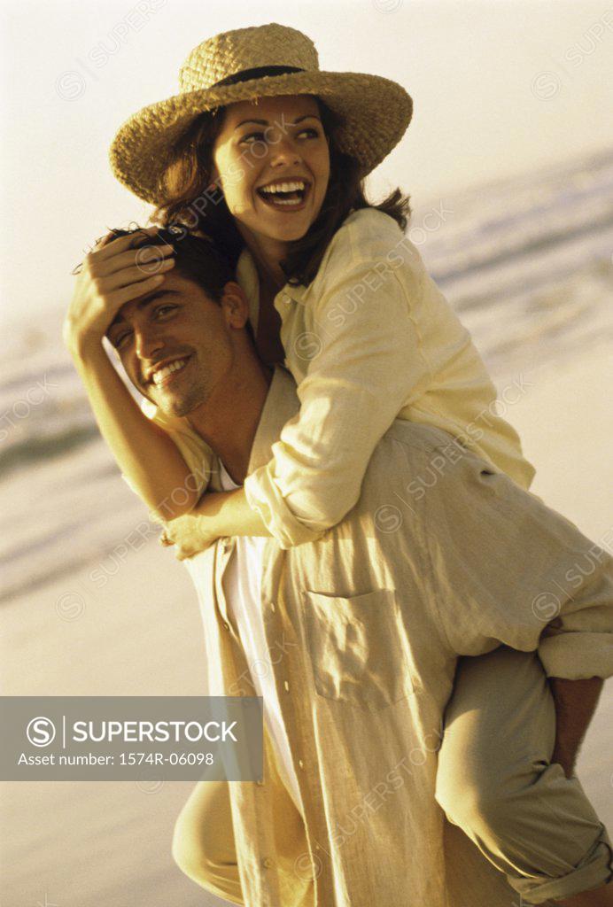 Stock Photo: 1574R-06098 Young woman riding piggyback on a young man on the beach