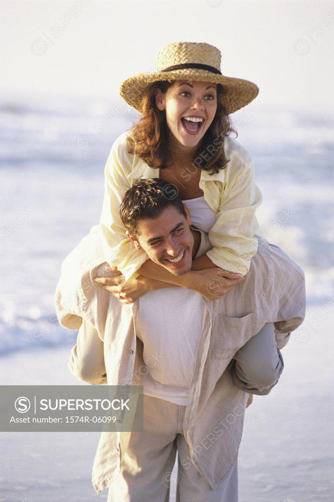 Stock Photo: 1574R-06099 Young woman riding piggyback on a young man on the beach