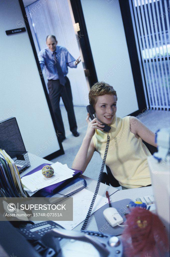 Stock Photo: 1574R-07351A Secretary talking on a telephone with a businessman standing in a doorway behind
