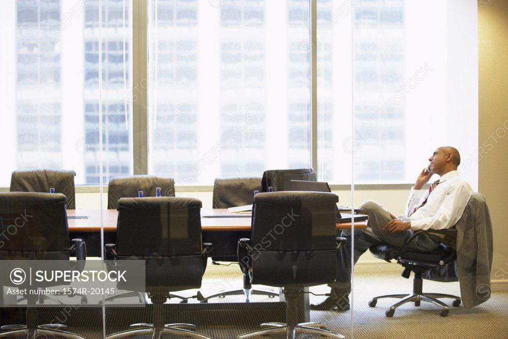 Stock Photo: 1574R-20145 Side profile of a businessman talking on a mobile phone in a board room