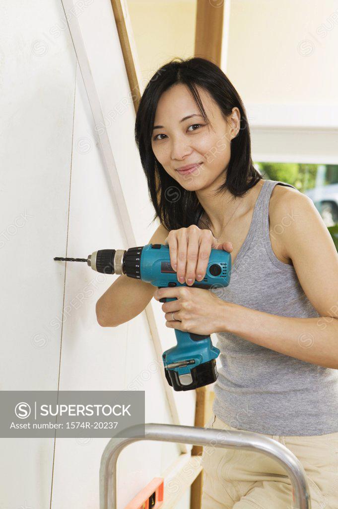 Stock Photo: 1574R-20237 Portrait of a young woman drilling into a wall