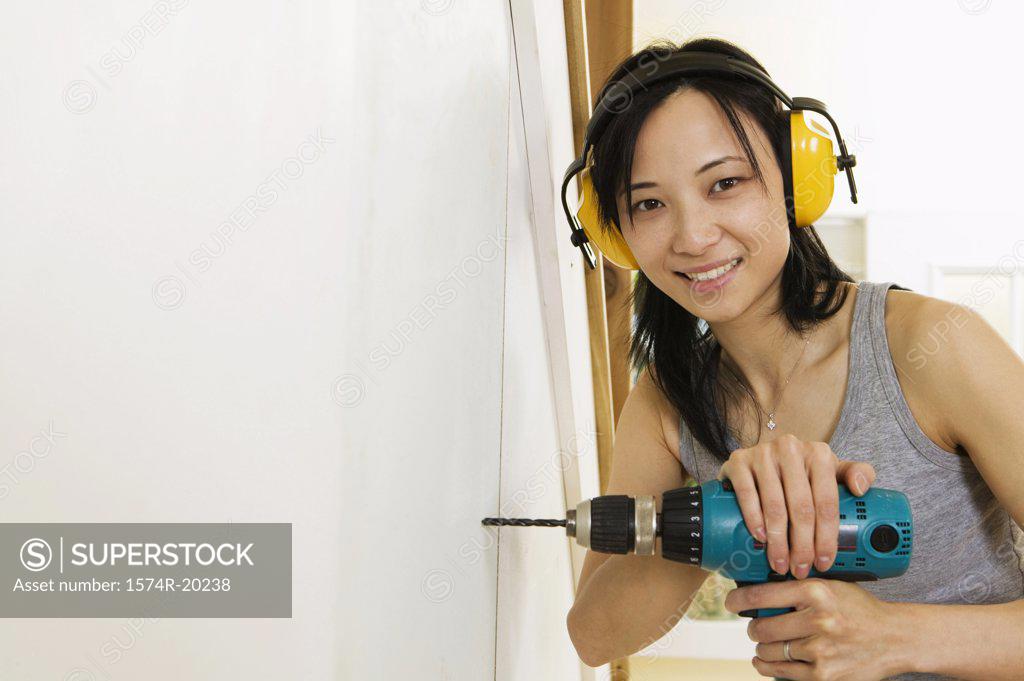 Stock Photo: 1574R-20238 Portrait of a young woman drilling into a wall