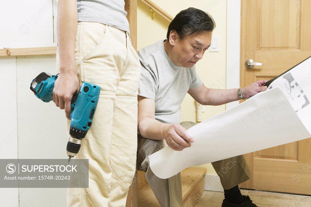 Stock Photo: 1574R-20243 Mid section view of a young woman holding a drill with a mid adult man looking at a blueprint