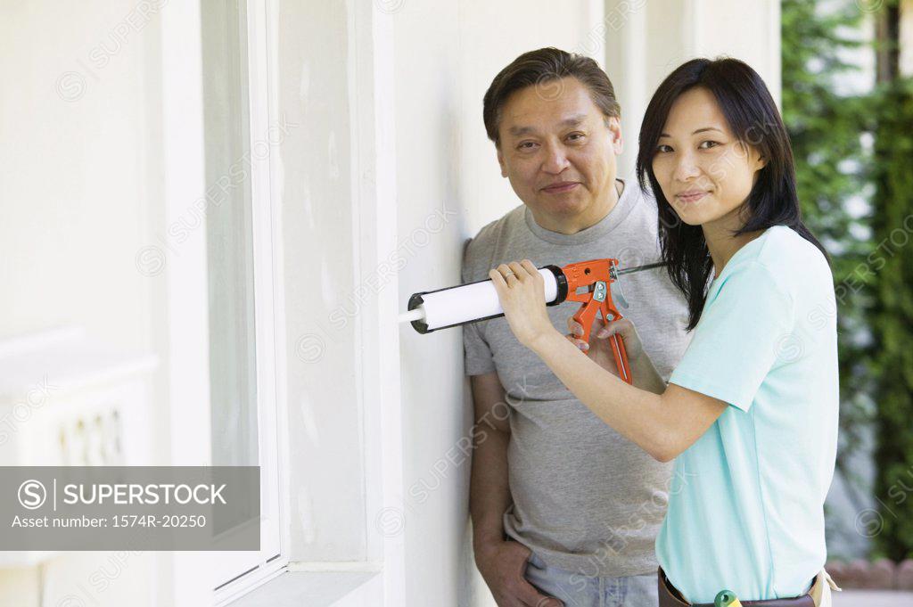 Stock Photo: 1574R-20250 Mid adult man standing with a young woman using a caulk gun