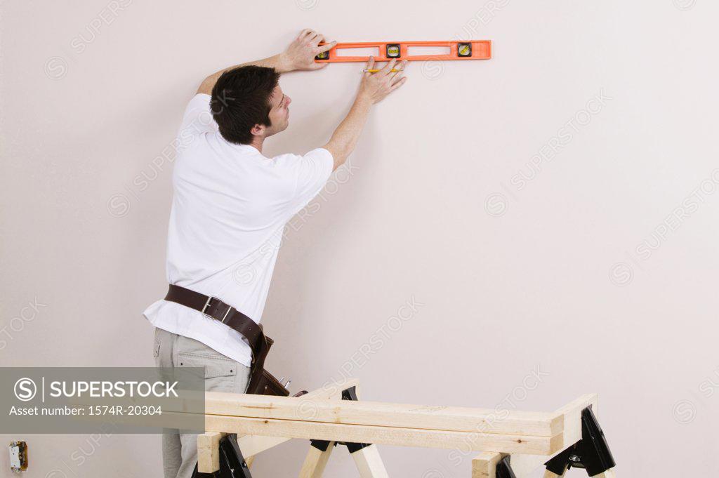 Stock Photo: 1574R-20304 Rear view of a young man using a spirit level to mark on a wall