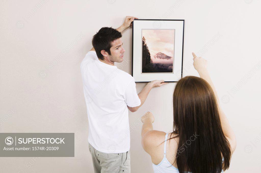 Stock Photo: 1574R-20309 Rear view of a young man putting up a painting on a wall with a young woman's guidance