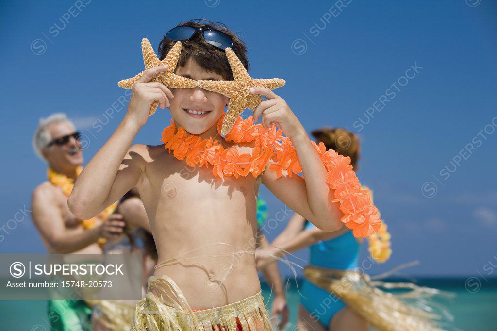Stock Photo: 1574R-20573 Close-up of a boy holding two starfish in front of his eyes with his grandparents and sister in the background