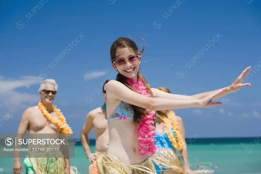 Close-up of a girl hula dancing on the beach with her grandparents and father standing in the background