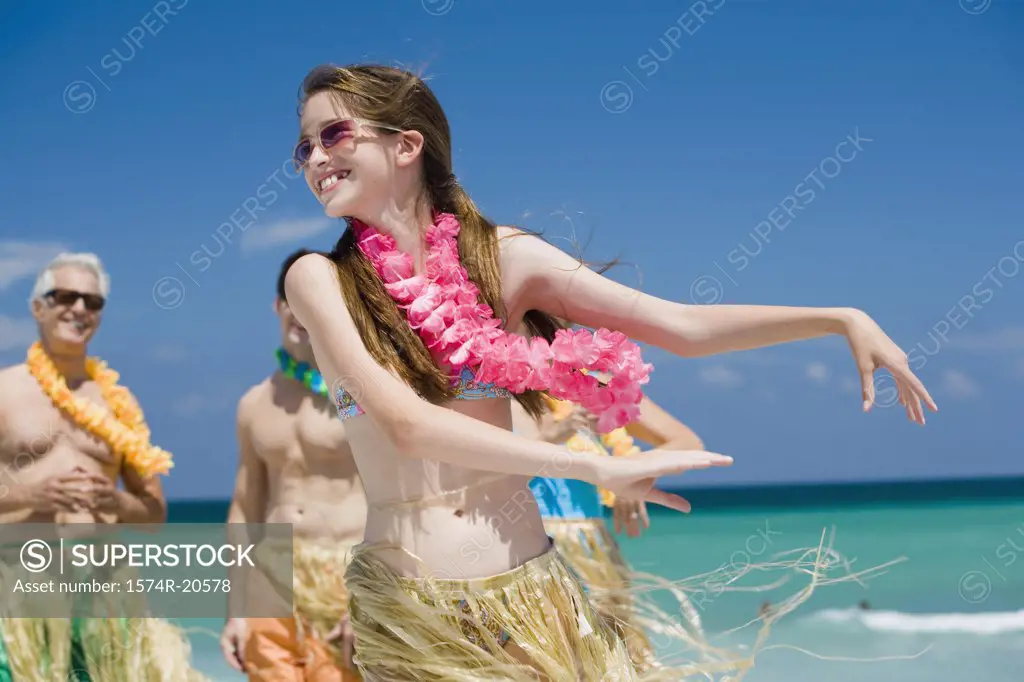 Close-up of a girl hula dancing on the beach with her grandparents and father standing in the background
