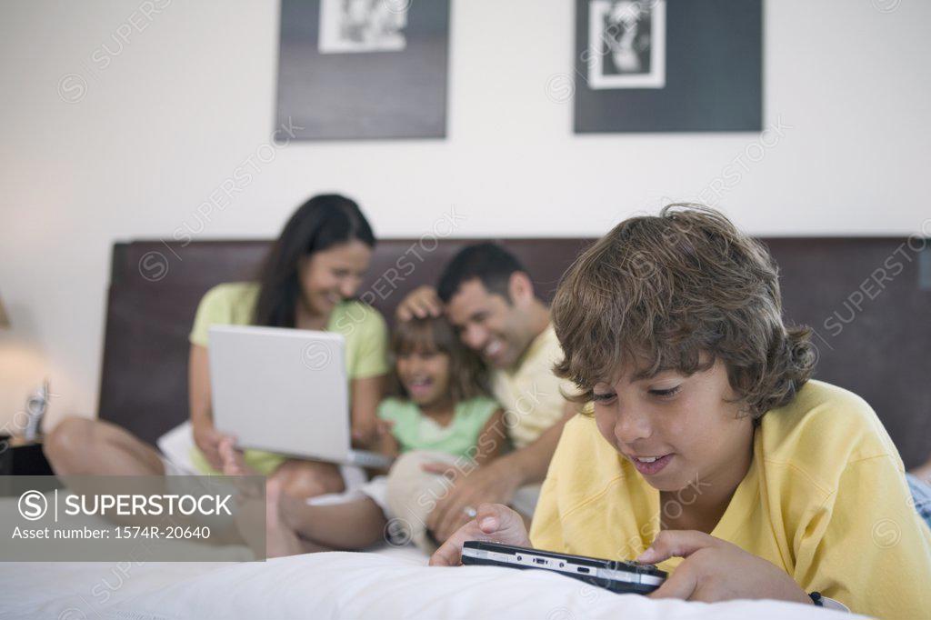 Stock Photo: 1574R-20640 Close-up of a boy playing a video game in the bed and his parents and sister behind him