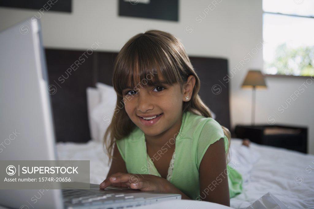 Stock Photo: 1574R-20656 Portrait of a girl lying in the bed and using a laptop