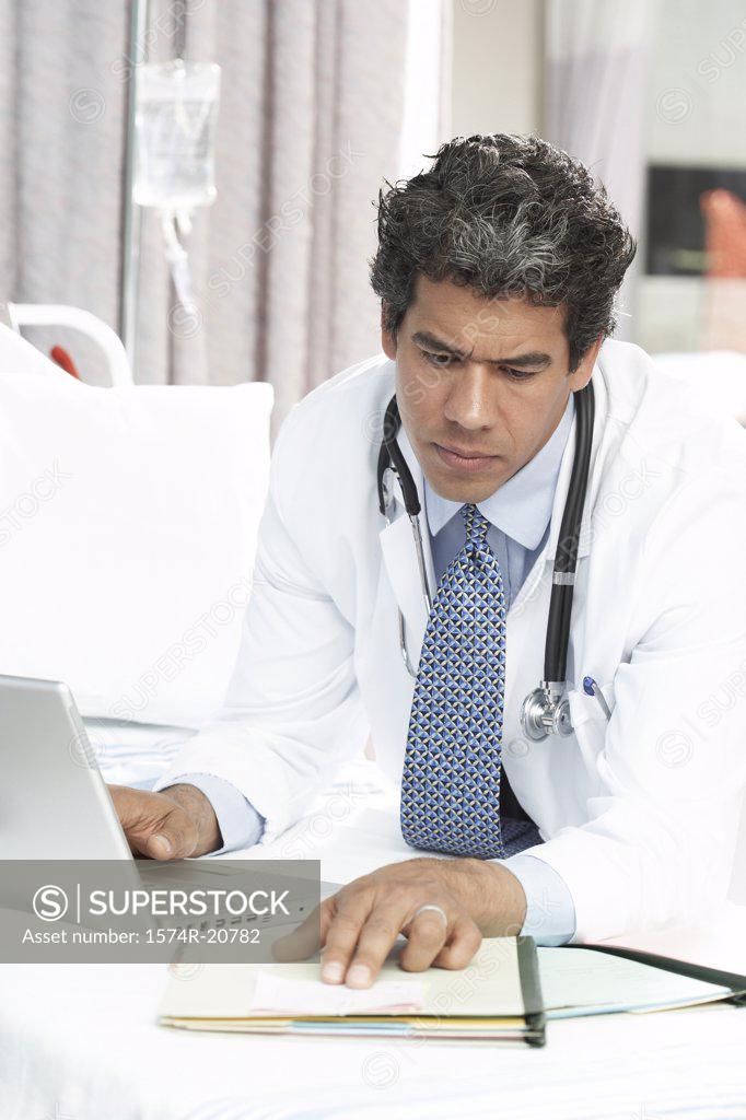 Stock Photo: 1574R-20782 Close-up of a male doctor using a laptop while reading a document