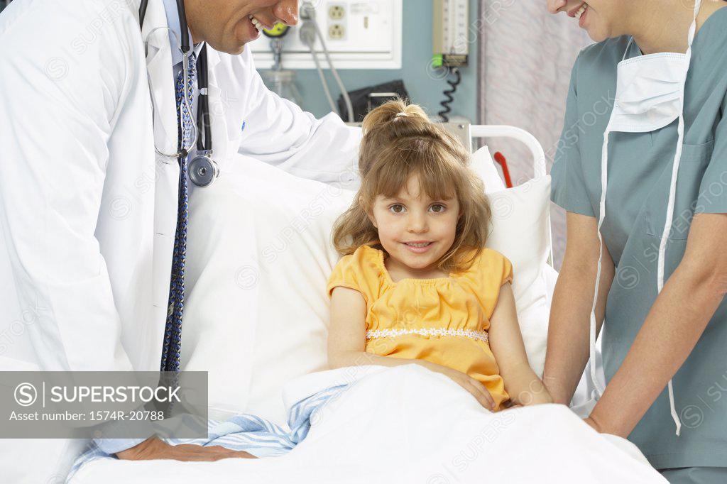 Stock Photo: 1574R-20788 Portrait of a girl sitting on the bed with a nurse and a male doctor standing beside her