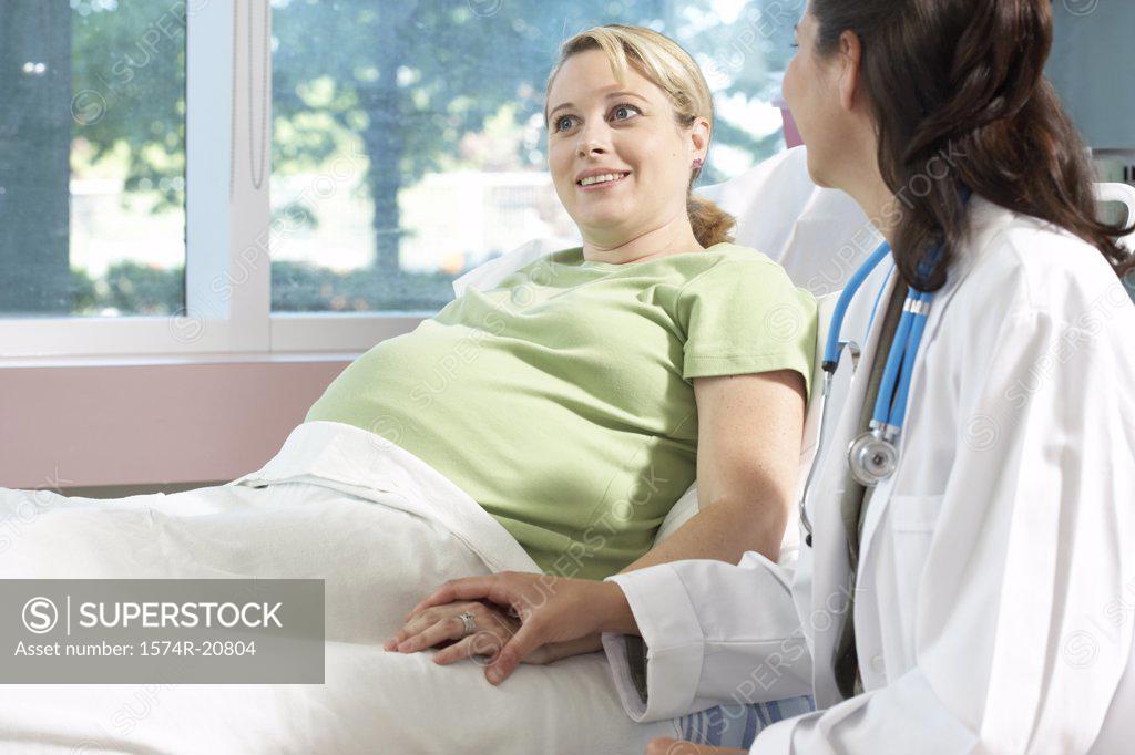 Stock Photo: 1574R-20804 Pregnant woman reclining on the bed with a female doctor sitting beside her