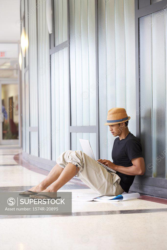 Stock Photo: 1574R-20895 Side profile of a college student sitting in a corridor and using a laptop