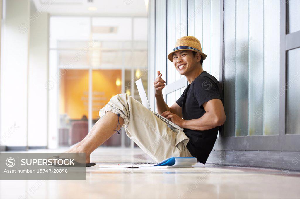 Stock Photo: 1574R-20898 College student sitting in a corridor with a laptop on his lap