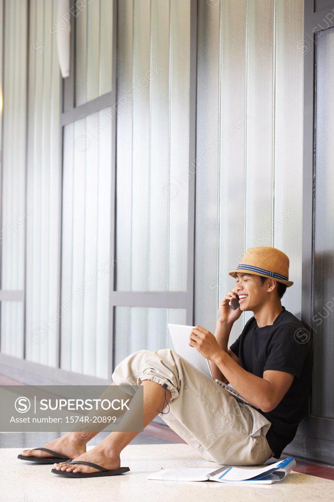 Stock Photo: 1574R-20899 Side profile of a college student sitting in a corridor and talking on a mobile phone