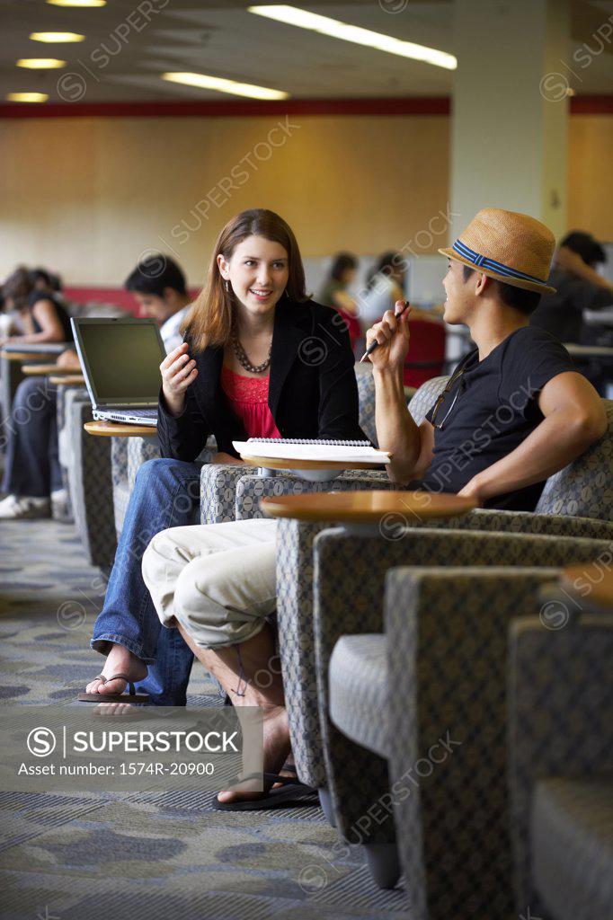 Stock Photo: 1574R-20900 Side profile of two college students sitting in a lecture hall and talking to each other