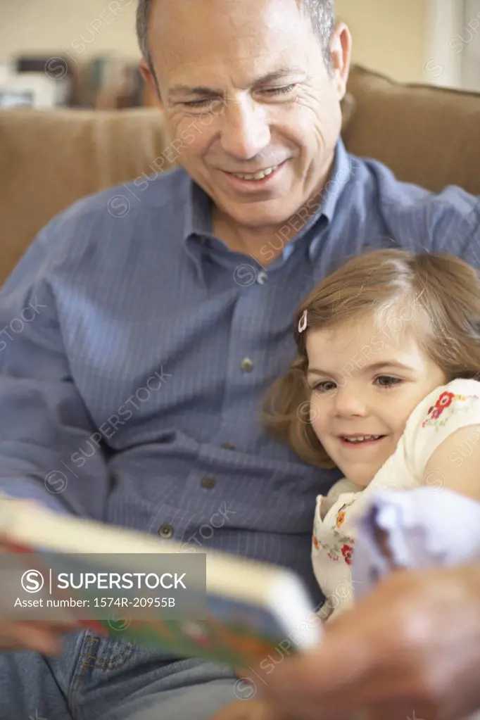 Close-up of a girl sitting with her grandfather and reading a book
