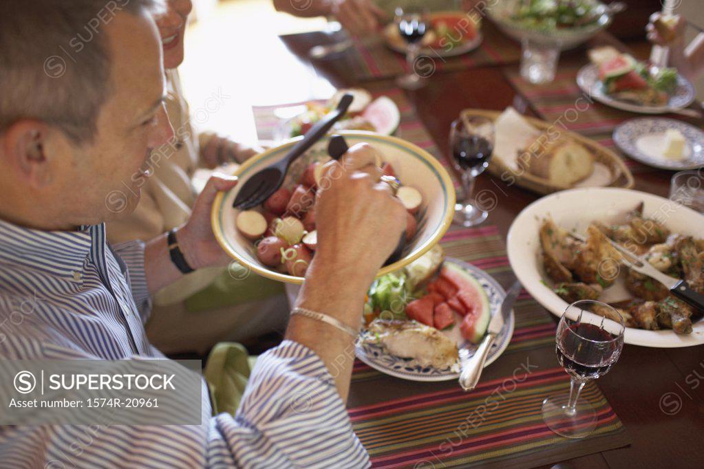 Stock Photo: 1574R-20961 High angle view of a mature man holding a vegetable bowl at a dining table