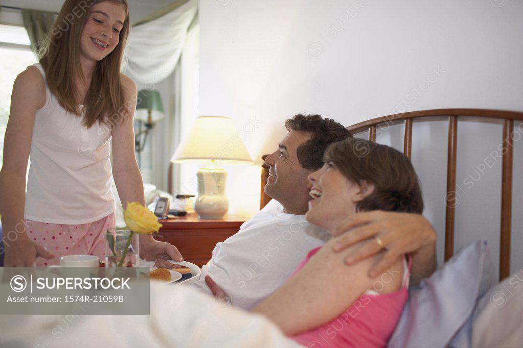 Stock Photo: 1574R-21059B Side profile of a mid adult couple in the bed with their daughter holding a tray standing beside the bed