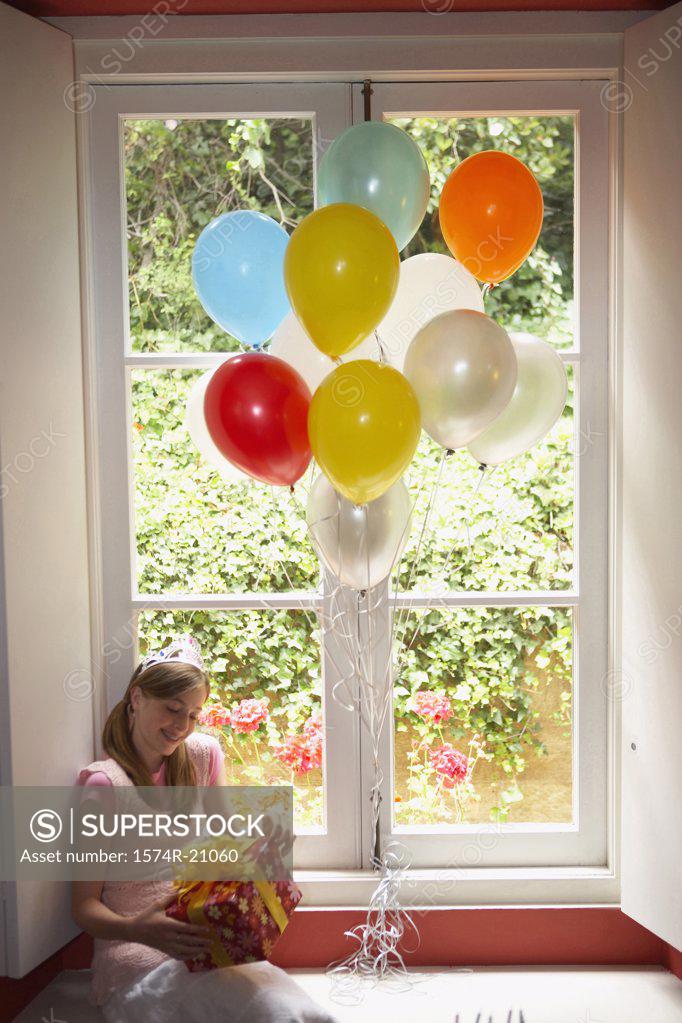 Stock Photo: 1574R-21060 High angle view of a teenage girl sitting on a window ledge and holding her birthday present