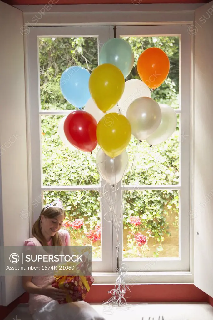 High angle view of a teenage girl sitting on a window ledge and holding her birthday present