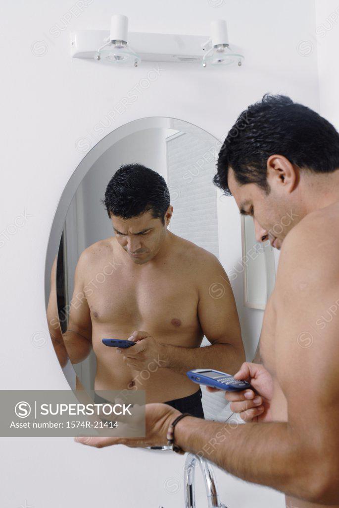 Stock Photo: 1574R-21414 Side profile of a mid adult man standing in front of a mirror and using a mobile phone in the bathroom