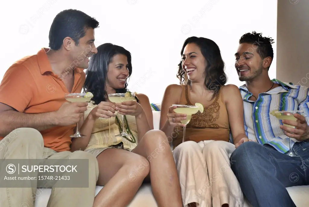 Mid adult couple and a young couple sitting on a couch and holding margaritas