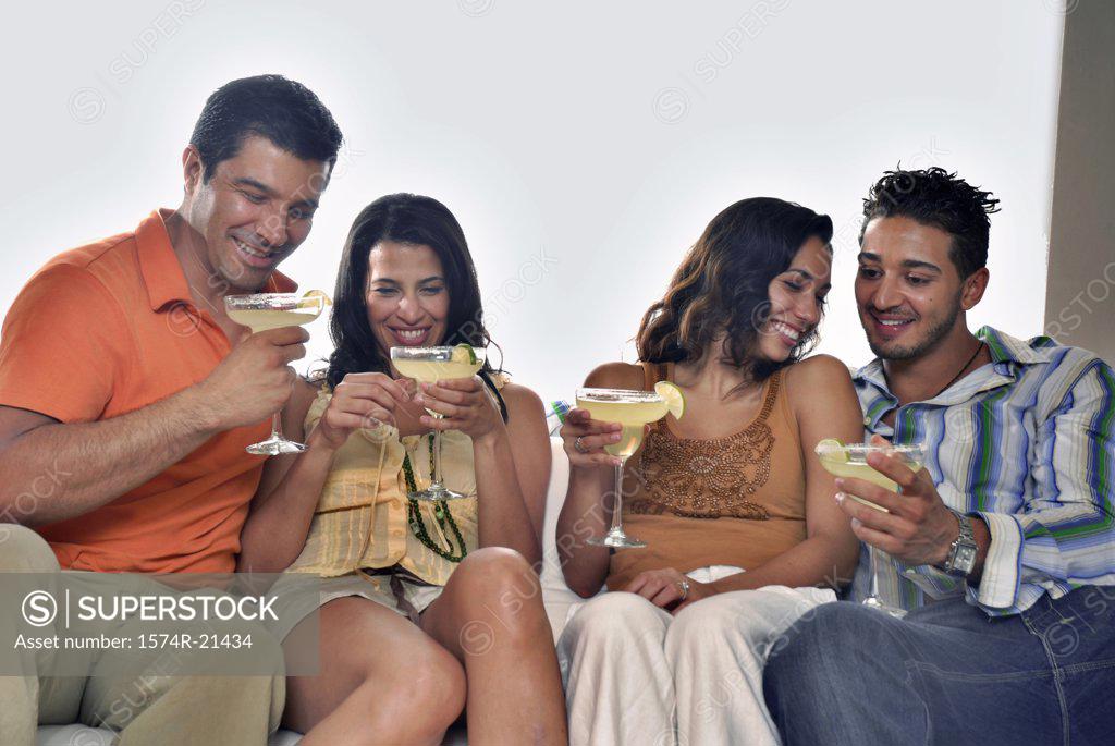 Stock Photo: 1574R-21434 Mid adult couple and a young couple sitting on a couch and holding margaritas
