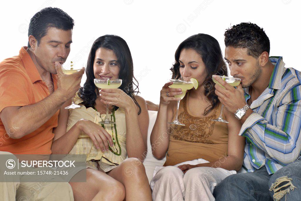 Stock Photo: 1574R-21436 Mid adult couple and a young couple sitting on a couch and drinking margaritas