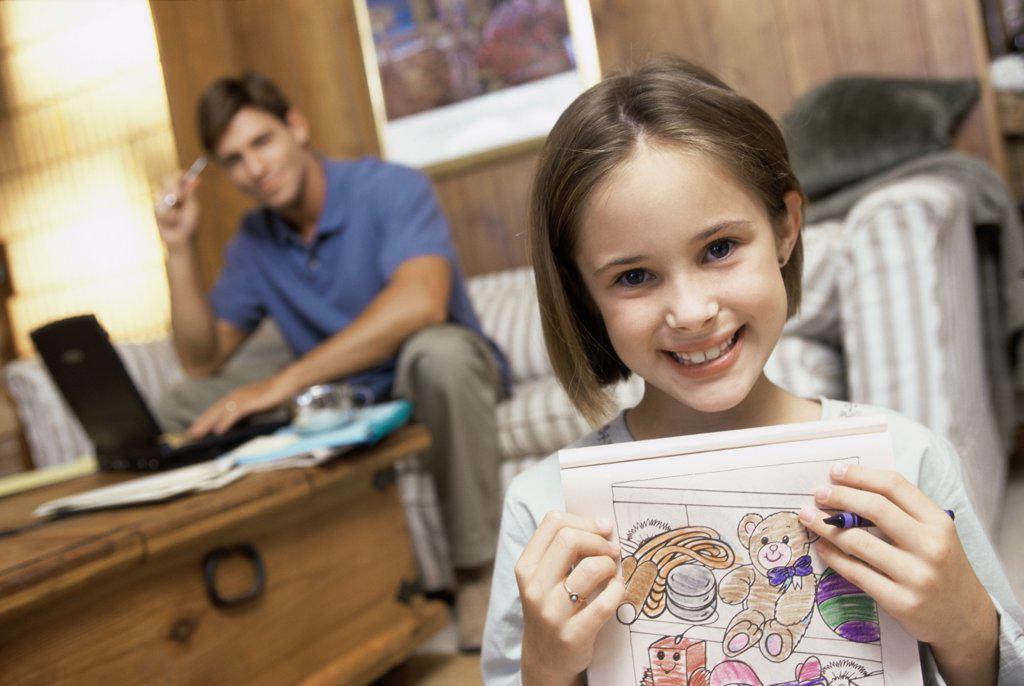 Portrait of a girl showing her drawing with her father sitting behind her