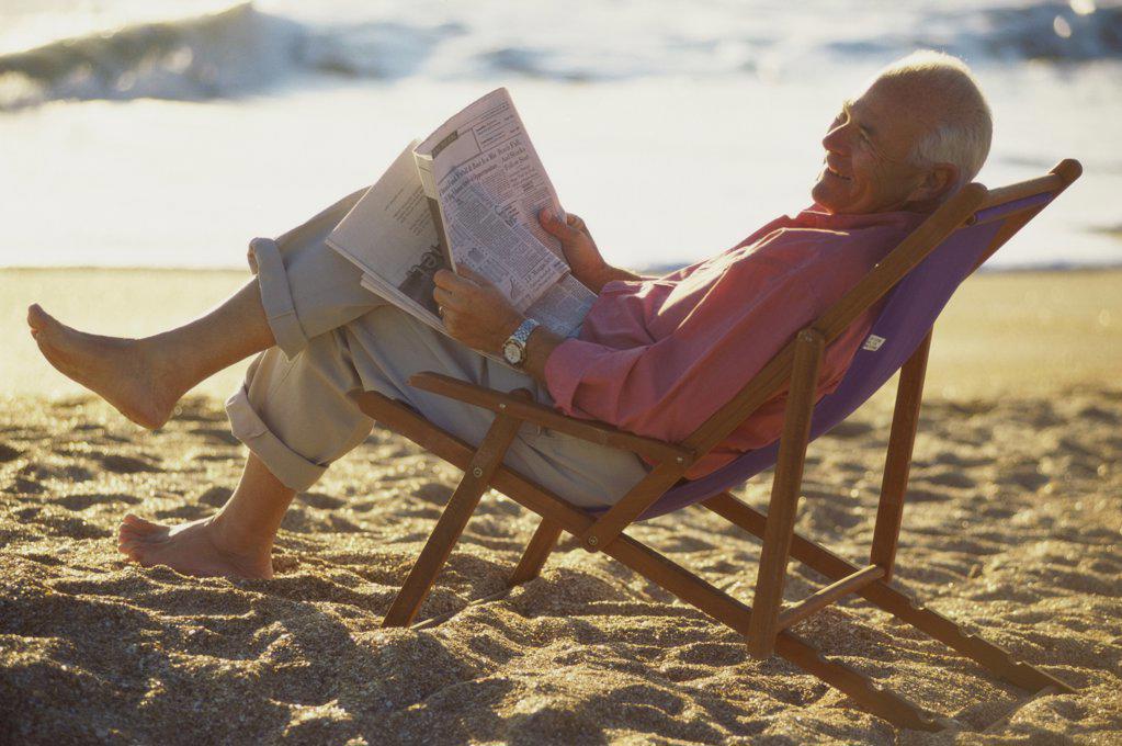 Side profile of a senior man reading a newspaper on the beach