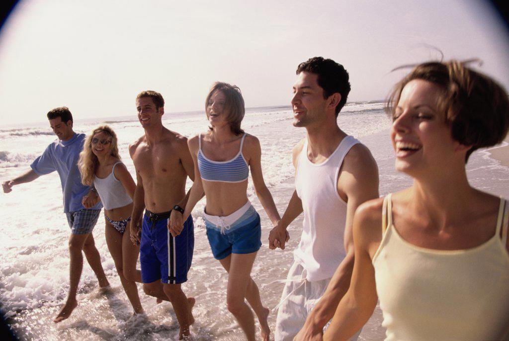 Three young couples holding hands walking on the beach