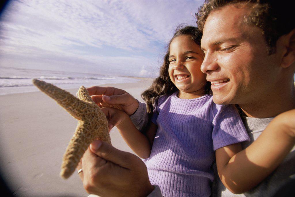 Close-up of a man showing his daughter a starfish on the beach