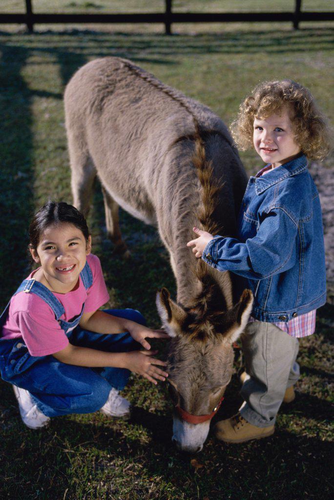 Portrait of two girls petting a donkey