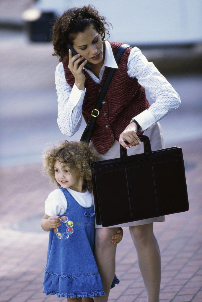 Mother talking on a mobile phone with her daughter standing beside her
