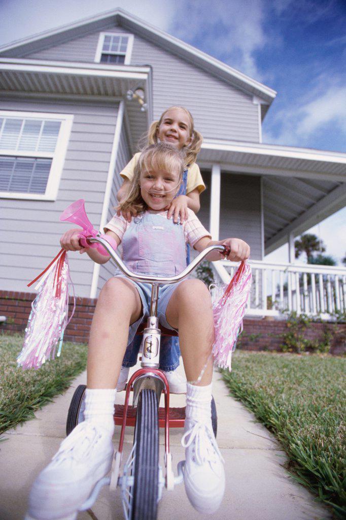 Portrait of two girls riding a tricycle