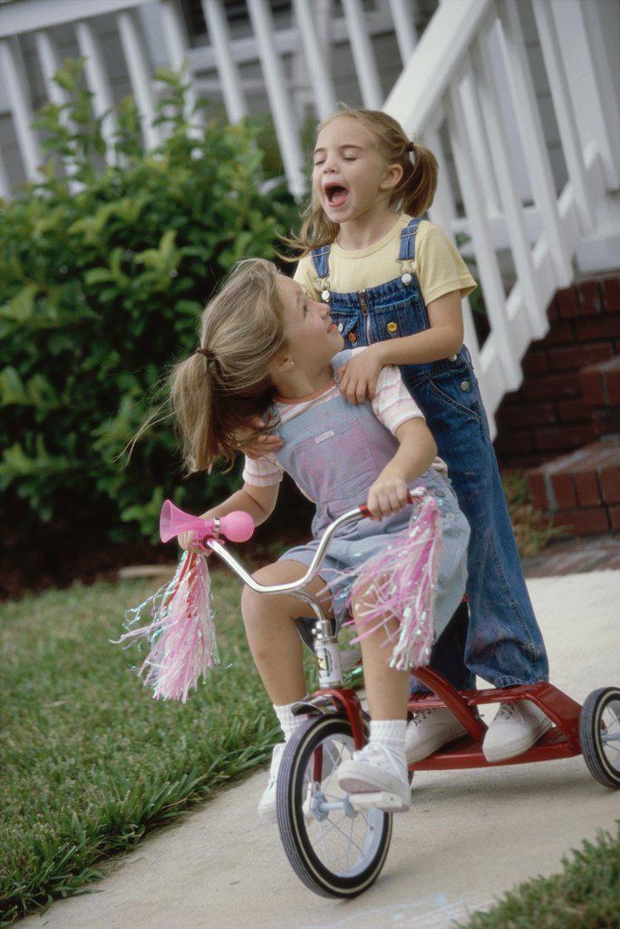 Two girls playing on a tricycle