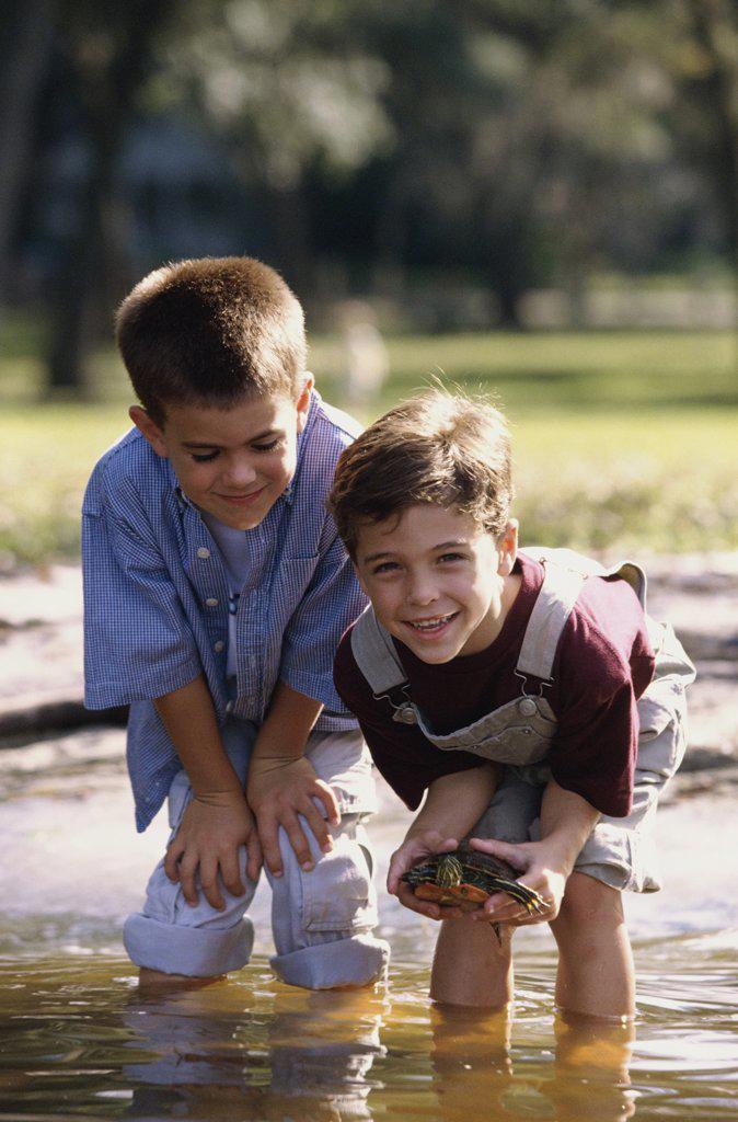 Portrait of two boys standing in water holding a turtle