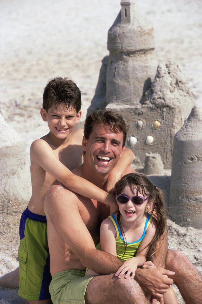 Portrait of a father with his son and daughter sitting on the beach