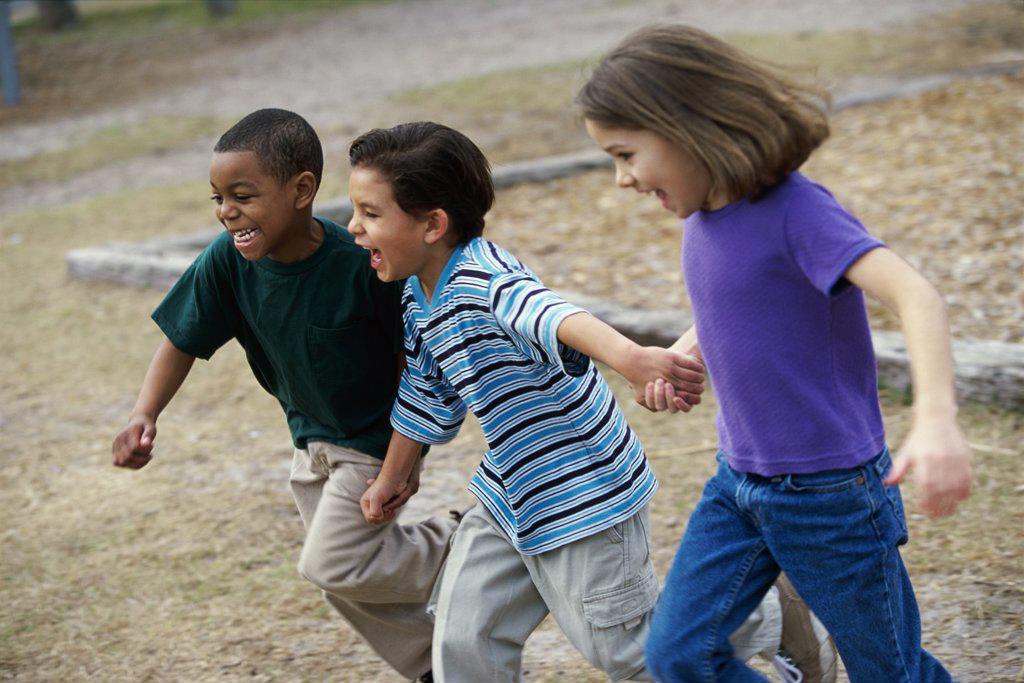 Side profile of two boys and a girl running holding hands