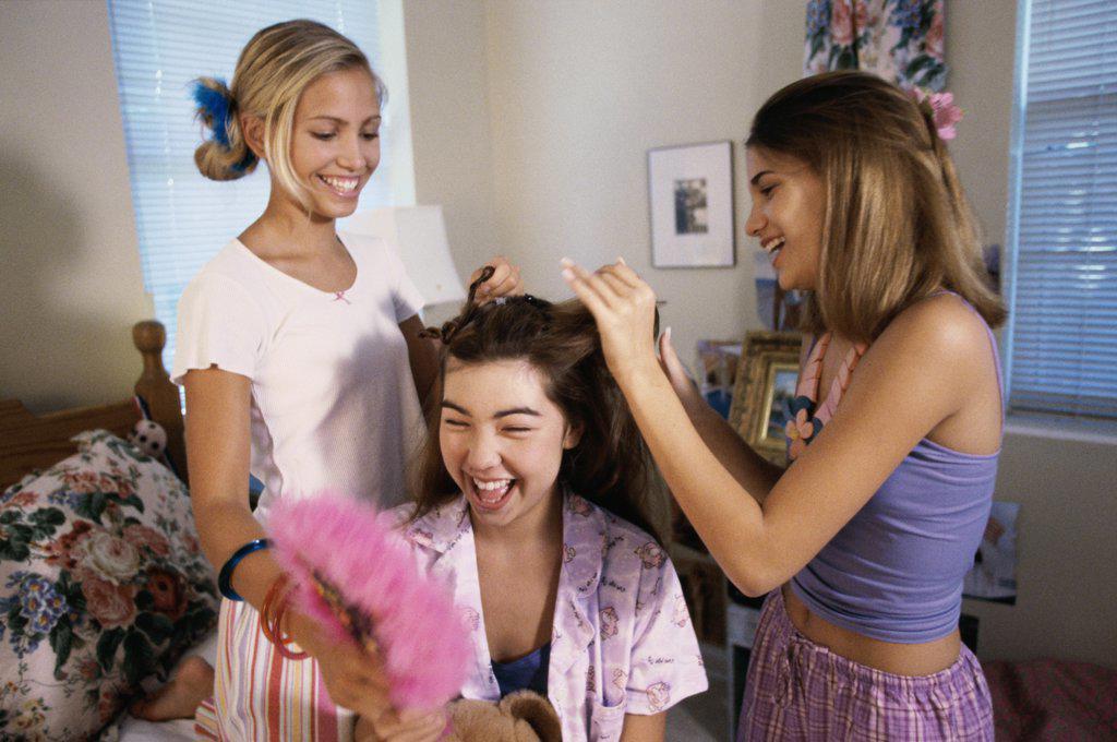 Two teenage girls styling their friend's hair
