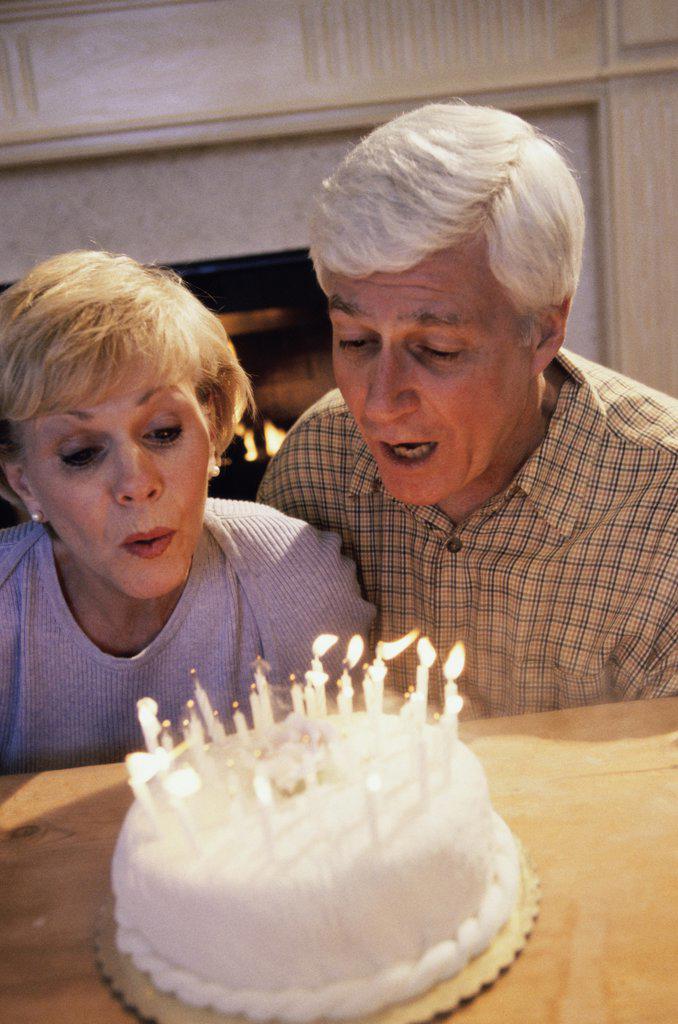 Senior couple blowing out candles on a cake