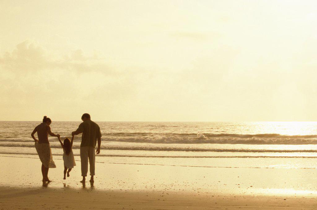 Silhouette of parents with their daughter on the beach