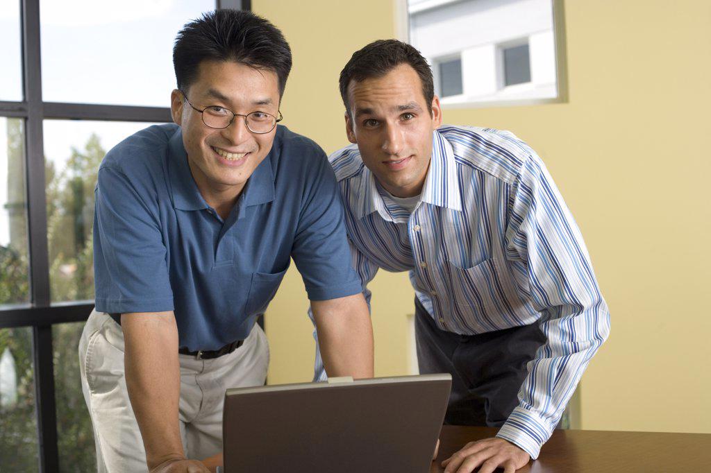 Portrait of two businessmen standing in front of a laptop