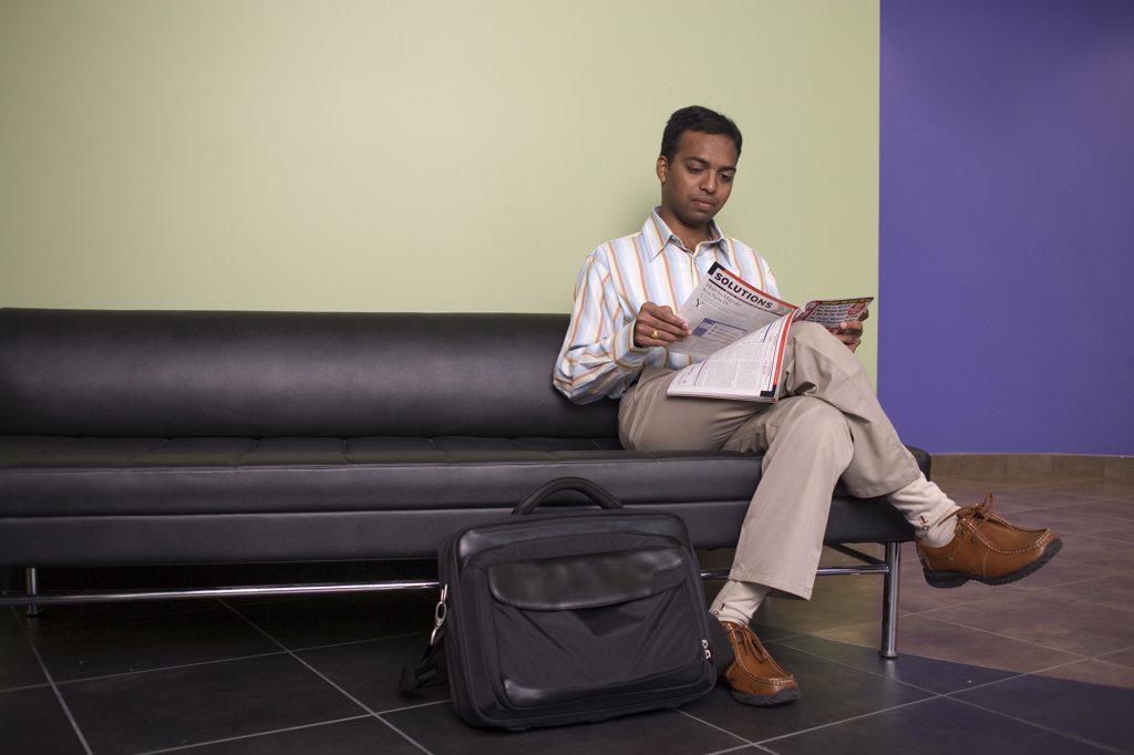 Businessman sitting on a couch reading a magazine in an office